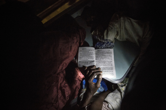 A woman reads a Hausa romance novel using the flashlight on her cell phone on a train crossing Nigeria. Image (c) Glenna Gordon